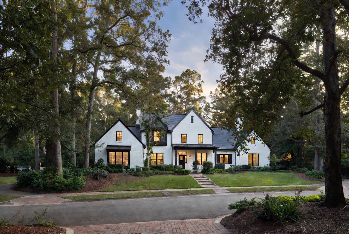 A white brick luxury home set back on a tree-lined street in Alpharetta, Georgia at dusk