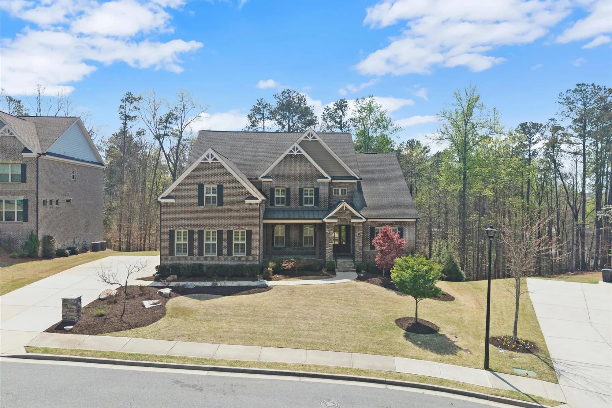 Front exterior of the stone-and-brick traditional estate with a manicured lawn and wooded backdrop — 5365 Briarstone Ridge Way, Alpharetta