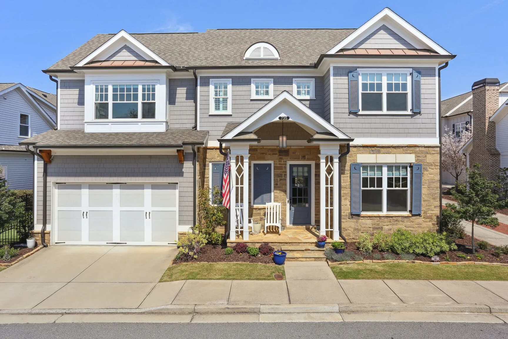 Front exterior of 735 Belle Isle Drive — a gray Craftsman home with stone accents, a covered front porch, and a two-car garage in Downtown Alpharetta's East of Main community.