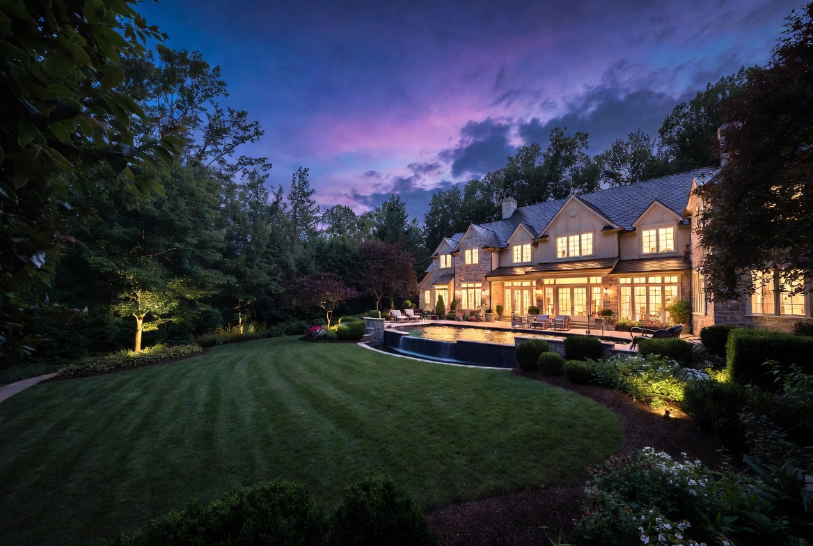 A stone-and-shingle luxury estate at twilight with warm window light, a lit pool, and a manicured lawn in North Fulton, Georgia